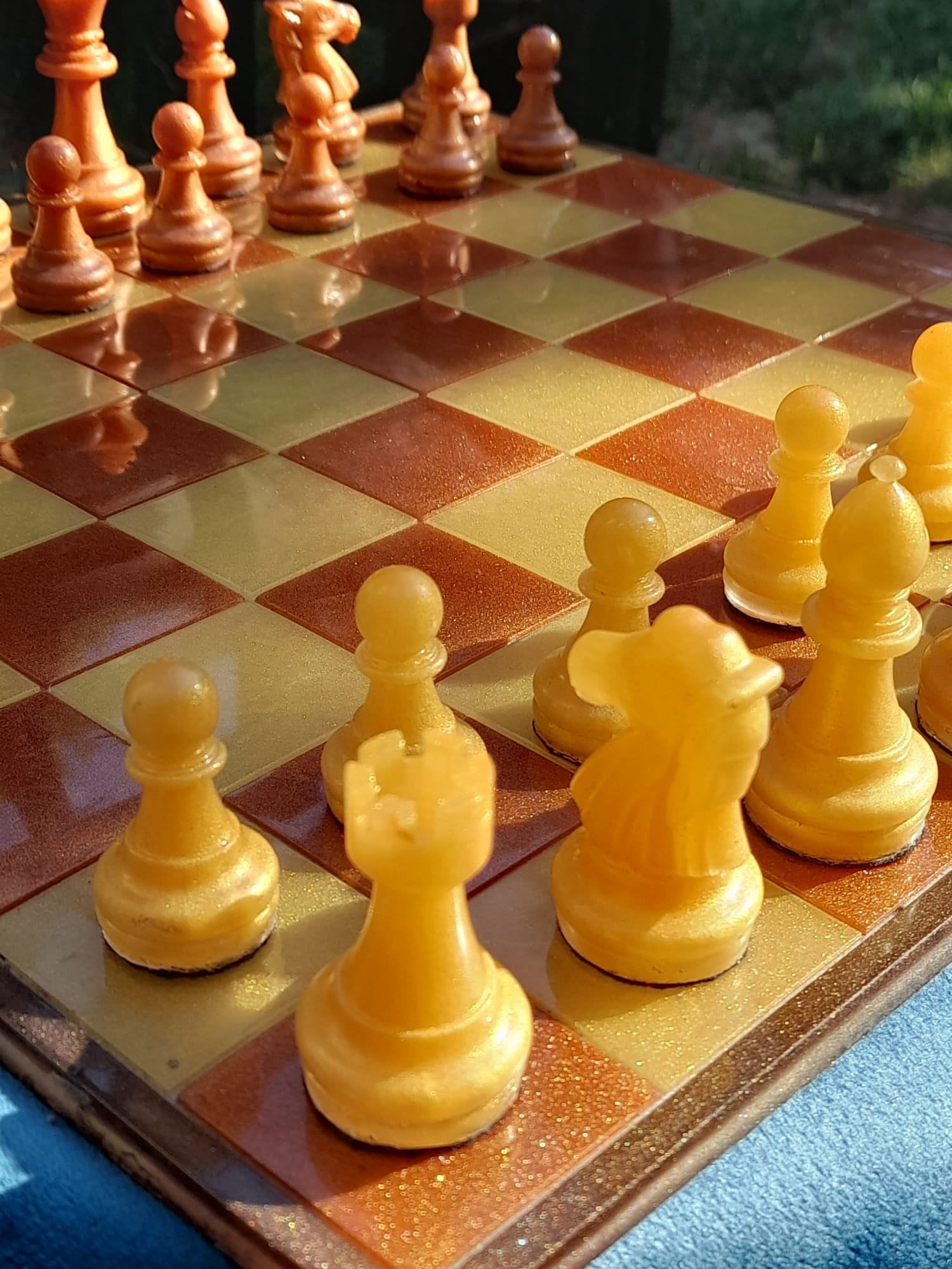 Close-up of amber and yellow resin chess pieces on glittery resin board, outdoor setting
